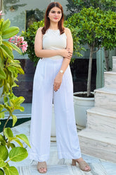 Woman in a white outfit standing outdoors with greenery and steps in the background