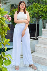 Woman in a white outfit standing outdoors with greenery and steps in the background