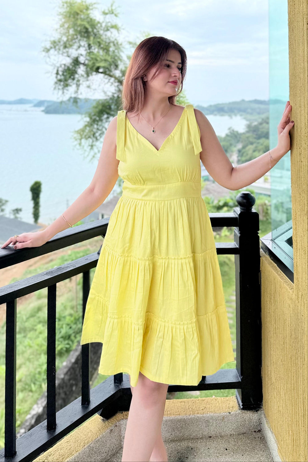 Woman in a yellow dress standing on a balcony with a scenic view.