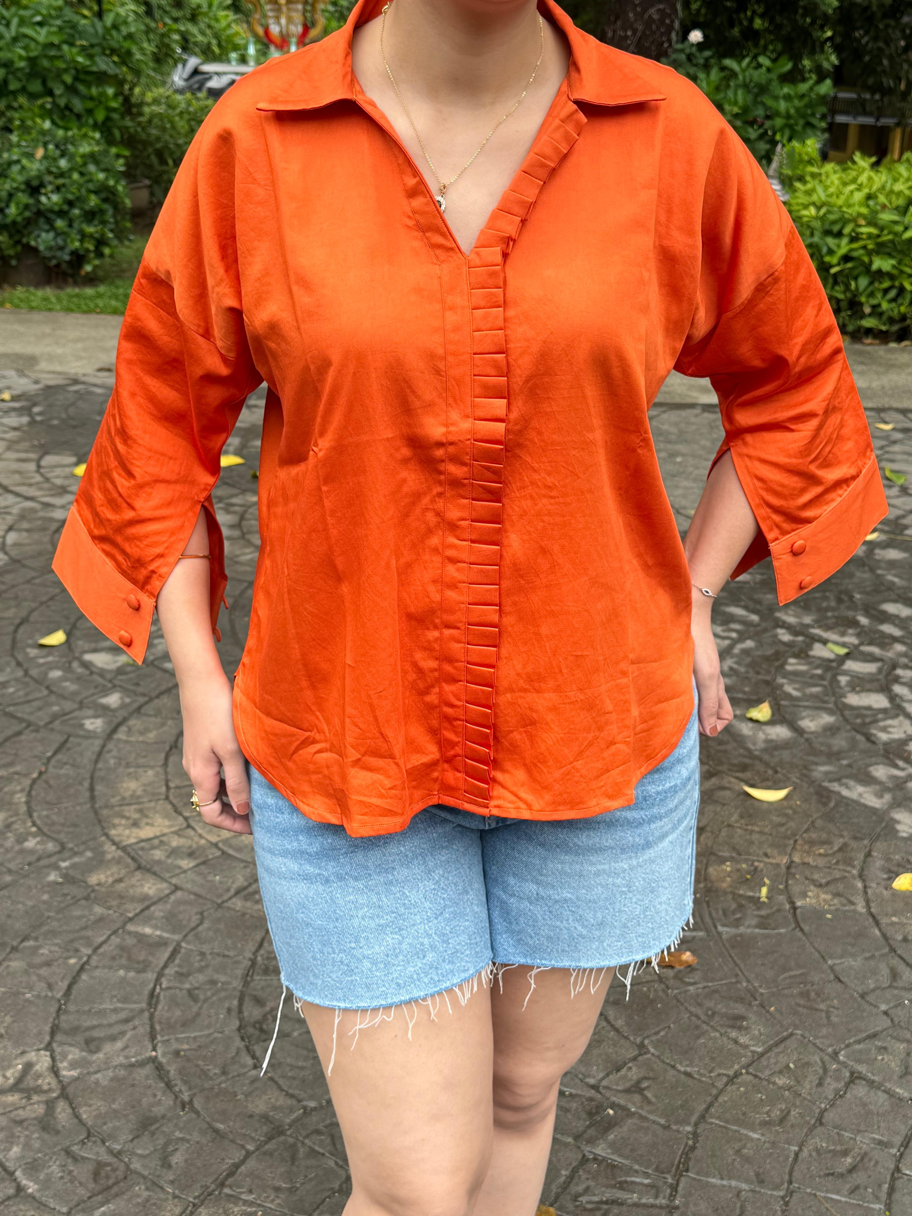 Person wearing an orange shirt and denim shorts on a stone pavement.